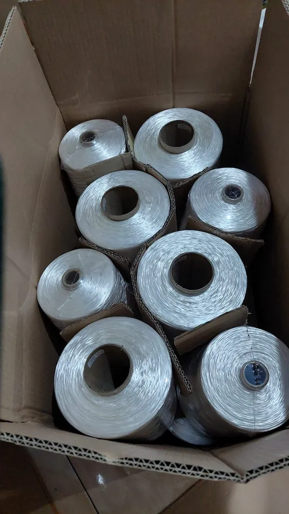 Delapan cone benang putih tertata dalam dus karton