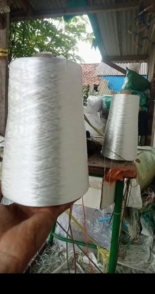 Cone benang polyester putih dipegang untuk perbandingan ukuran