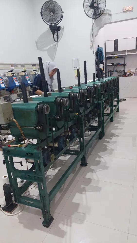 Deretan mesin twisting hijau dengan operator memantau penggulungan benang
