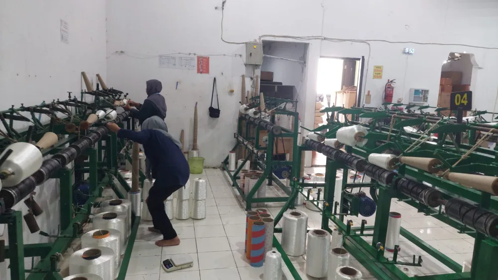 Dua operator memasang bobin benang pada mesin twisting stasiun 04