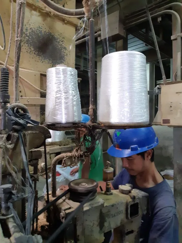 Operator ber-helm mengoperasikan mesin pemintal benang