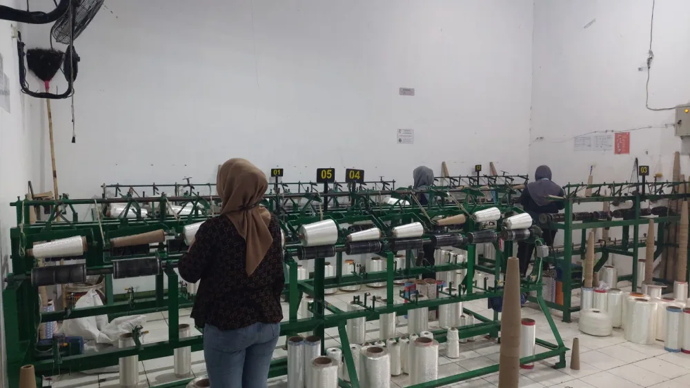 Operator mengawasi mesin twisting di antara deretan cone benang putih