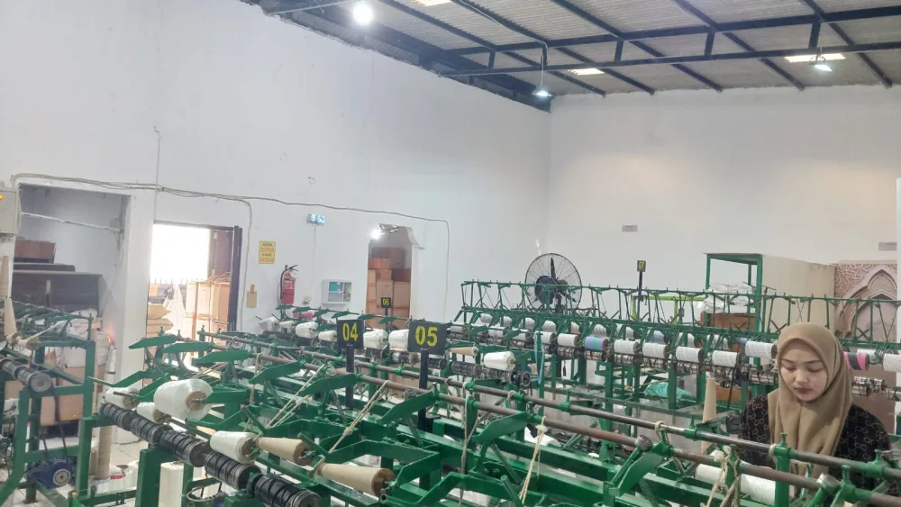 Ruang produksi dengan barisan mesin twisting hijau bernomor stasiun